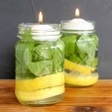 A homemade bug repellent candle with lemons and greenery inside of a mason jar.
