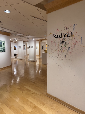 Radical Joy text displayed at the front of the gallery. Behind are works by various artists in the Radical Joy exhibition