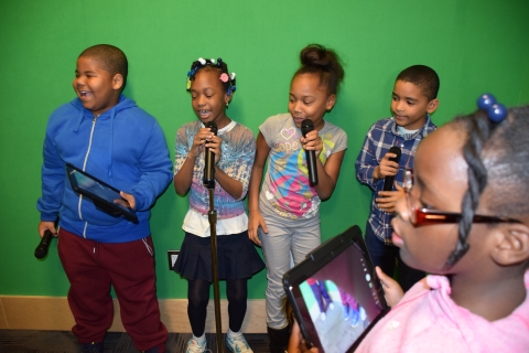 children singing in front of green screen wall