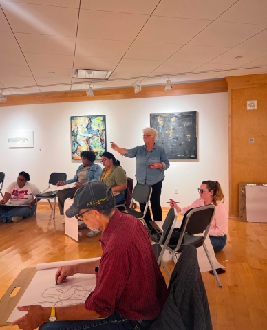 Library patrons seated and drawing looking at a model (out of picture) as the teacher explains drawing the human form.