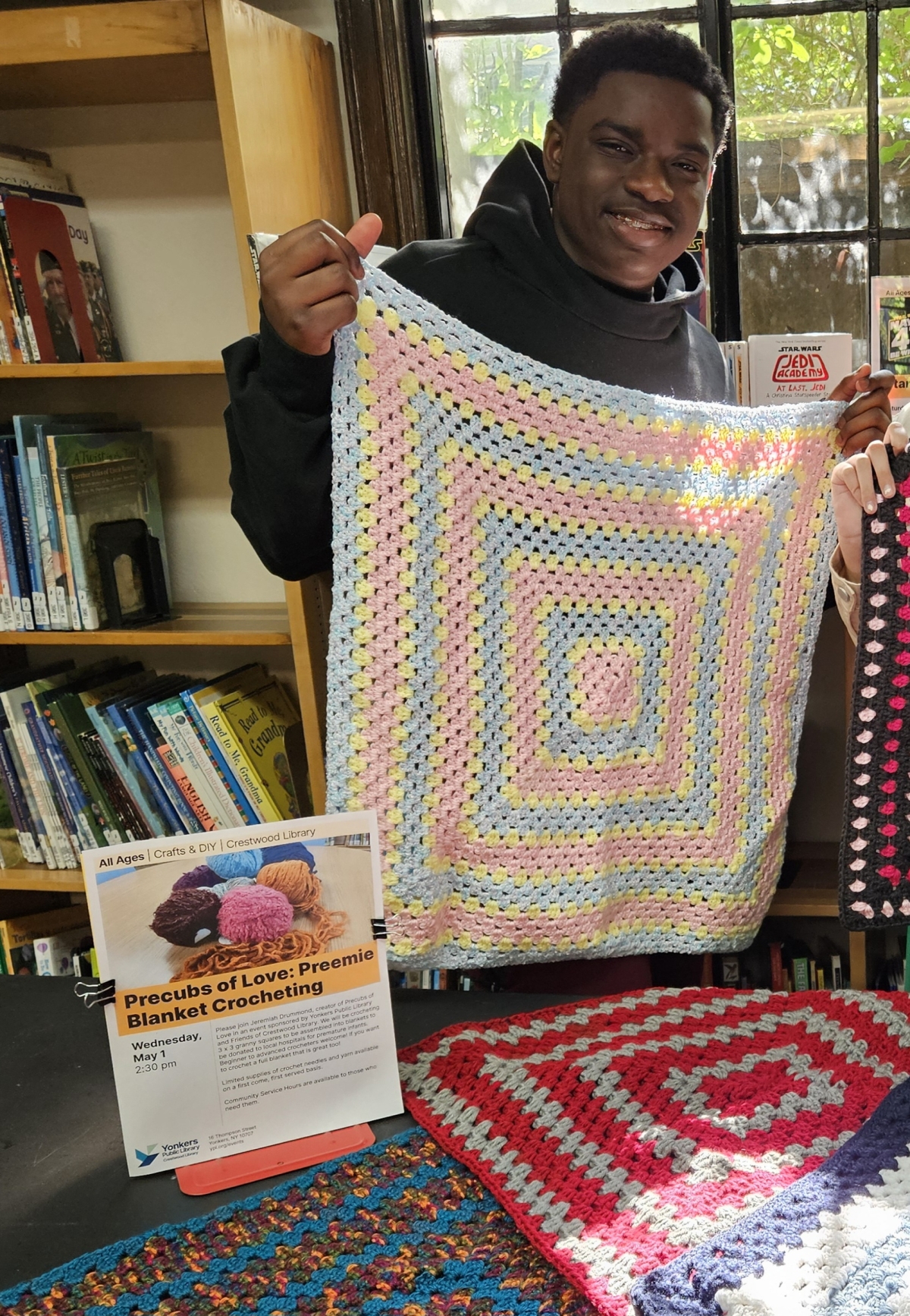 photo of jeremiah drummond holding up a completed crocheted blanket for preemies