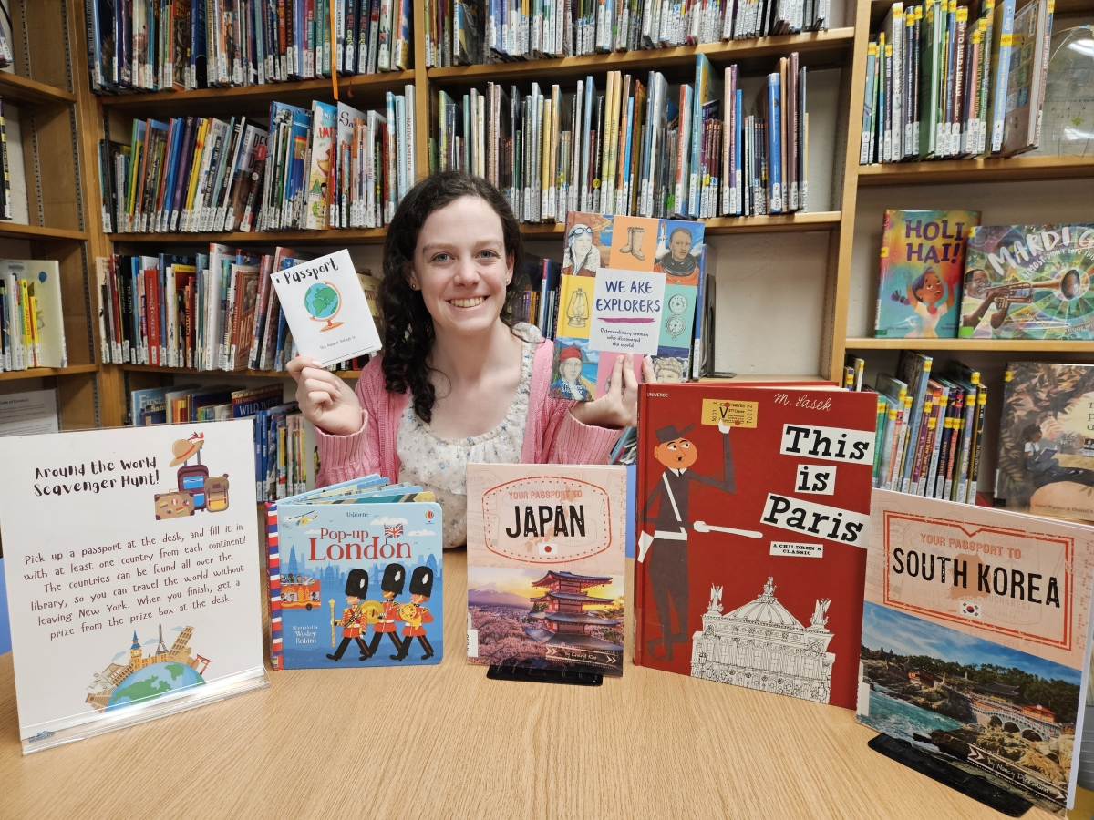 photo of Natalie holding up a passport and a book surrounded by travel books