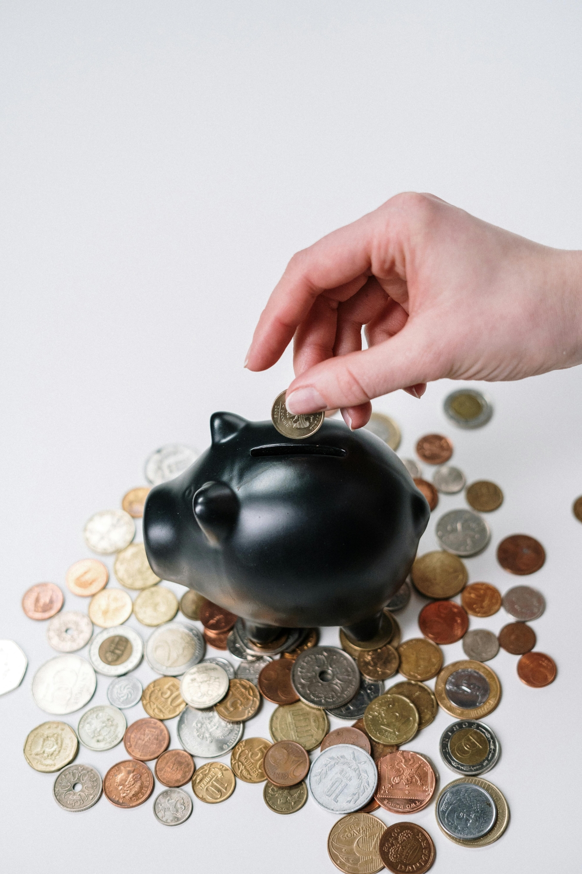 hand putting a coin in a piggy bank with coins around it photo credit cottonbro studio 