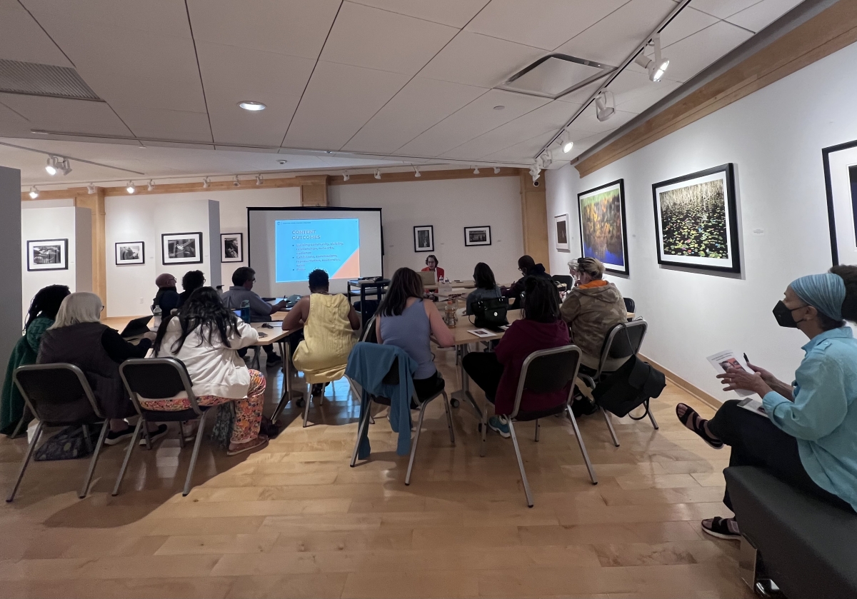 People sitting in chairs with their backs facing the camera, looking up at a presentation held on a projection screen.