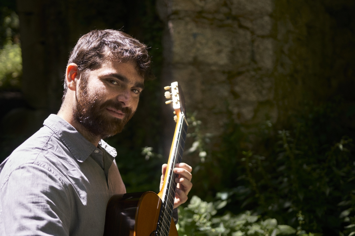 photo of Daniel Conant holding a guitar in a forest